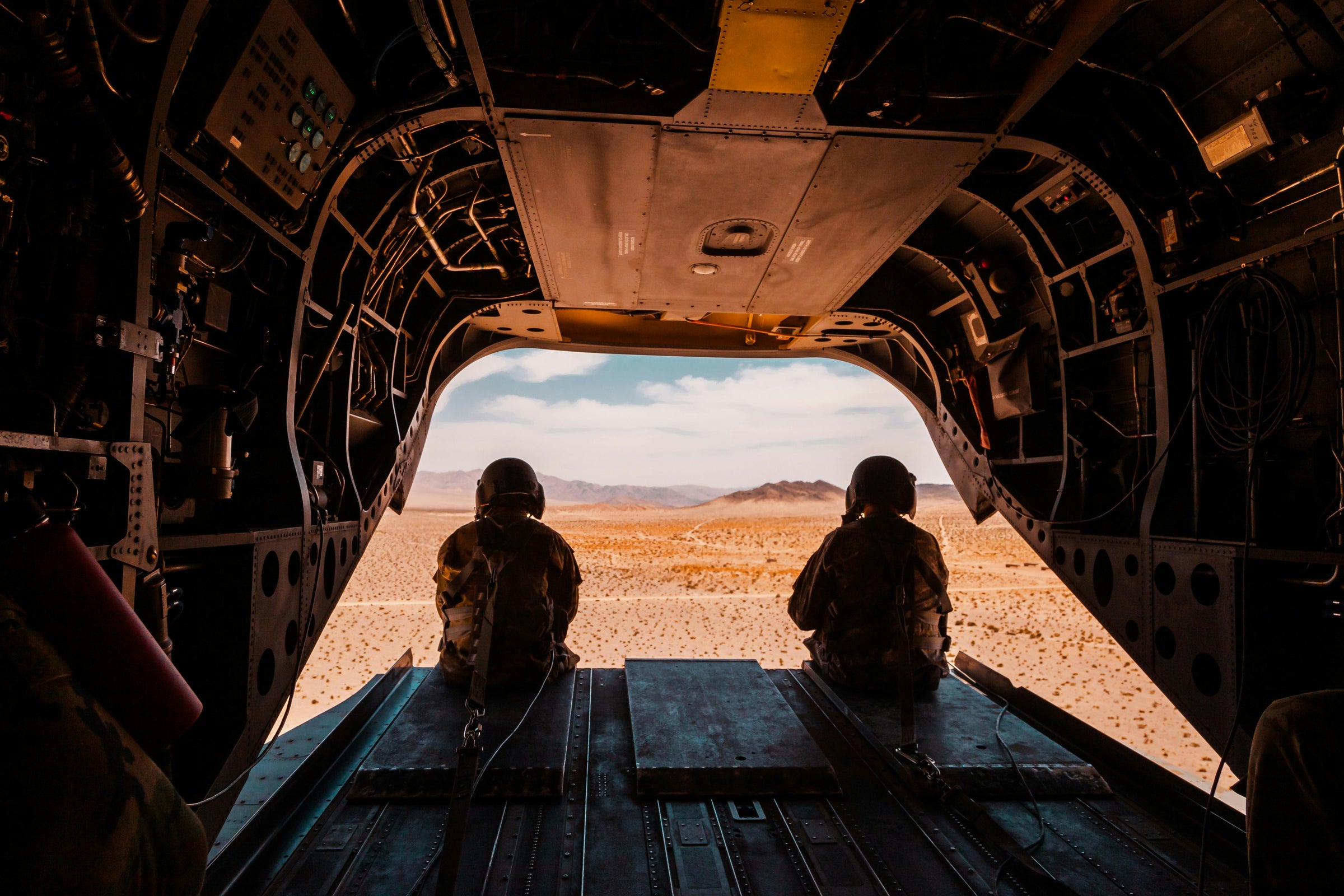 Two soldiers sitting inside an aircraft, looking out at a desert landscape.