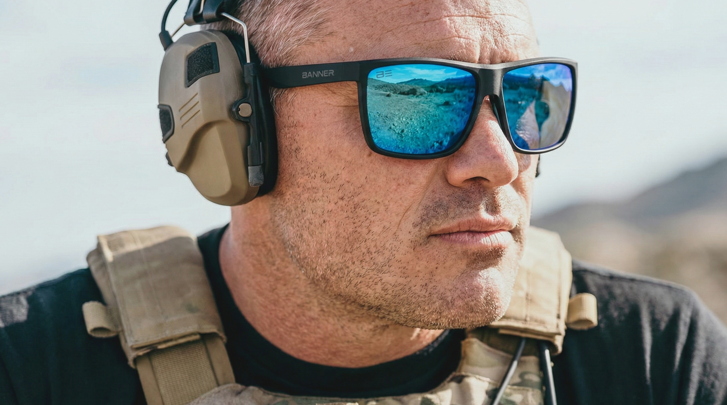 Person wearing tactical gear with reflective sunglasses and ear protection.