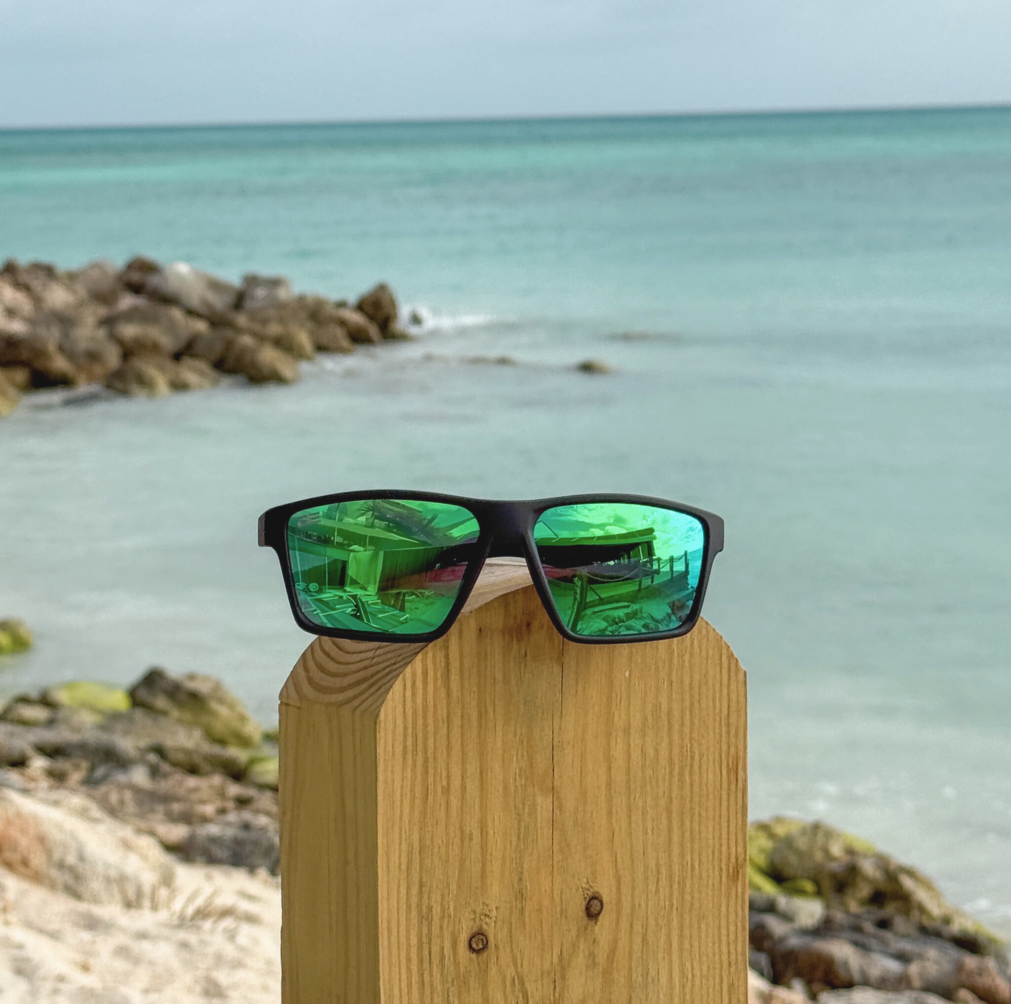 Sunglasses with green lenses on a wooden post by the ocean